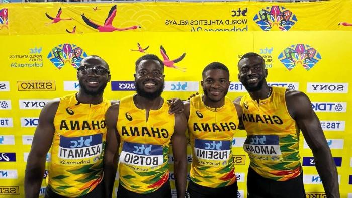 Four athletes pose before a yellow background, wearing their yellow Ghana jerseys and smiling with their arms around each other.